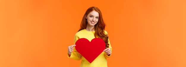 Wees mijn valentijn mooie prachtige roodharige krullende dwaze vriendin die een groot hartbord vasthoudt en glimlacht