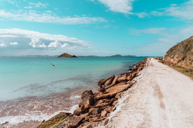 Weg bedekt met het zand, omringd door de zee en rotsen onder een blauwe hemel in Rio de Janeiro