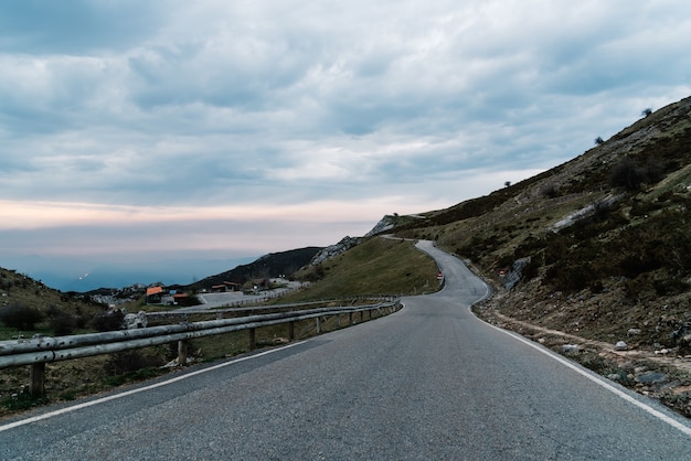 Weg omgeven door bergen onder een bewolkte hemel in de avond