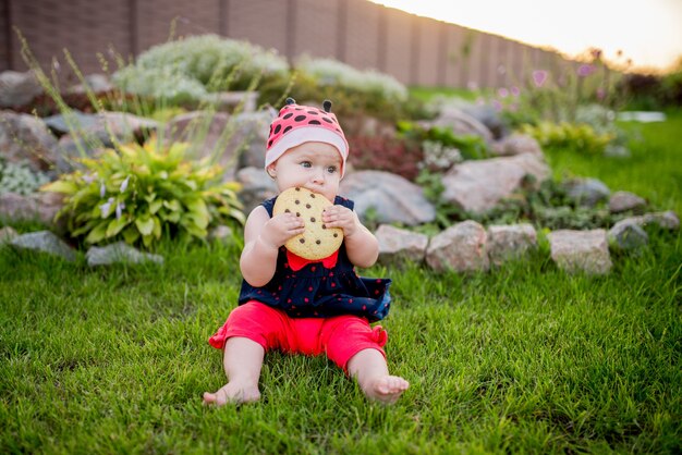 Weinig baby-meisje met een groot chocoladekoekje zit op de achtertuin
