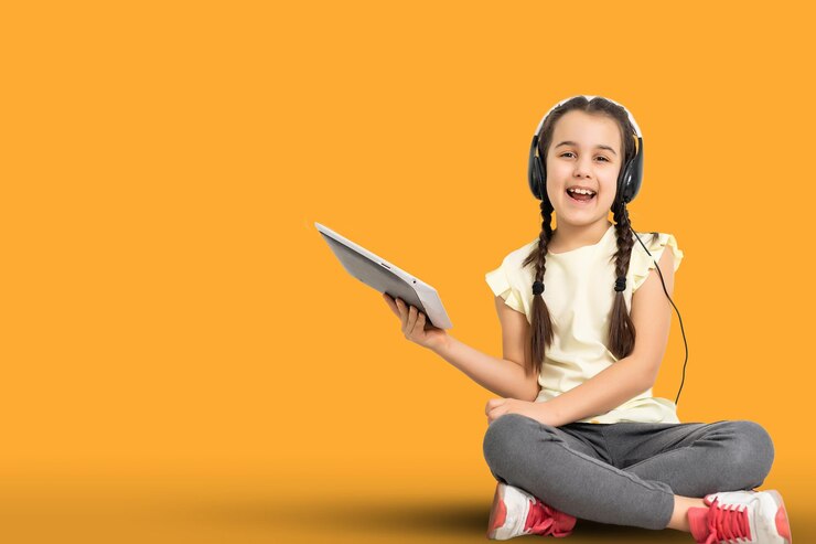 Weinig grappig meisje met tablet op gele studioachtergrond. Ze laat iets zien en wijst naar het scherm.
