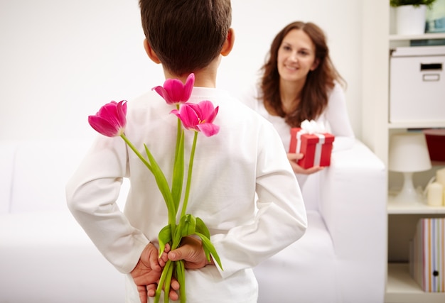 Weinig jongen met bloemen achter zijn rug