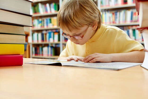 Weinig jongen met bril lezen in de bibliotheek