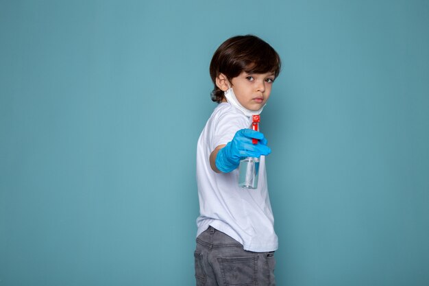 Weinig kindjongen met nevel in zijn handen tegen coronavirus in blauwe handschoenen op blauw bureau