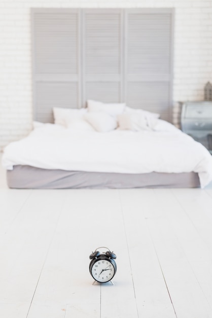 Gratis foto wekker op vloer dichtbij bed met wit linnen