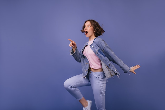 Welgevormd geschokt meisje dat in de verte kijkt. indoor foto van glamoureuze blanke vrouw in paarse broek.