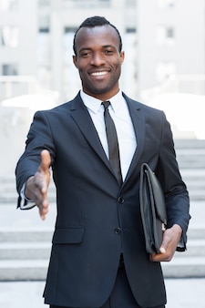 Welkom aan boord! knappe jonge afrikaanse man in volledig pak die zijn hand uitstrekt om te schudden terwijl hij buiten staat