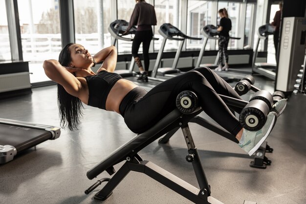 Welzijn. Jonge gespierde blanke vrouw oefenen in de sportschool met apparatuur. Atletisch vrouwelijk model dat ABS-oefeningen doet, haar bovenlichaam, buik opleidt. Wellness, gezonde levensstijl, bodybuilding.