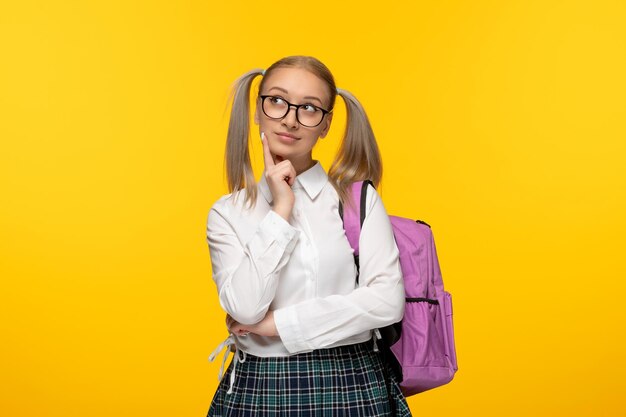 Wereldboekendag denkend schoolmeisje in glazen en roze rugzak op gele achtergrond