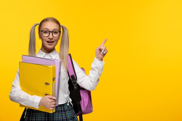 Wereldboekendag glimlachend gelukkig schoolmeisje met gele map en roze rugzak