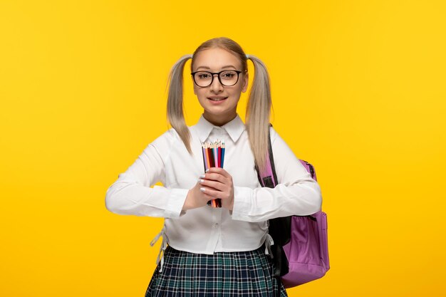 Wereldboekendag glimlachend juichend blond schoolmeisje met stapel kleurrijke potloden