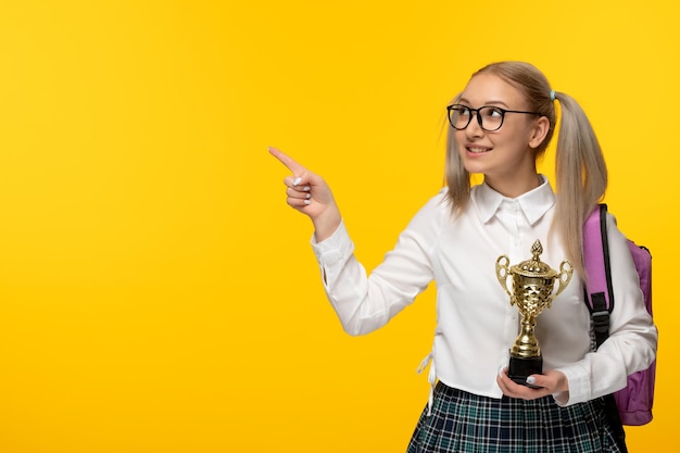 Wereldboekendag opgewonden gelukkig schoolmeisje dat naar links wijst met een gouden trofee