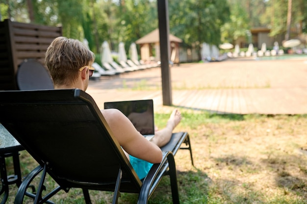 Werk en rust. Een man die op een chaise longue zit en op een laptop werkt