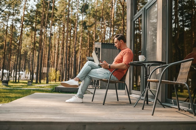 Werk vanuit huis. Een jonge man met een laptop die buiten zit en online werkt