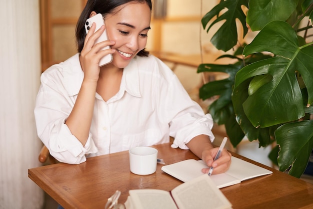 Werkende vrouw beantwoordt telefoontje in café en schrijft aantekeningen terwijl ze een gesprek voert op telep