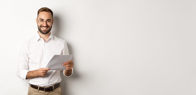 Werkgever die tevreden kijkt met het werk dat documenten leest en tevreden glimlacht terwijl hij over een witte achtergrond staat