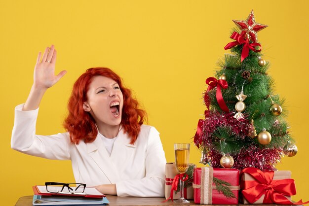 werkneemster zittend achter tafel met kerstboom en presenteert een beroep op geel