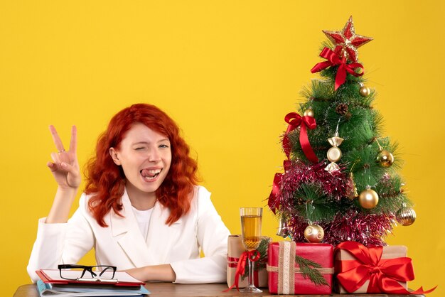 werkneemster zittend achter tafel met kerstcadeautjes en boom op geel