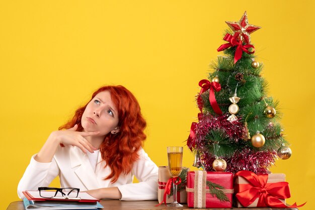 werkneemster zittend achter tafel met kerstcadeautjes en boom op geel