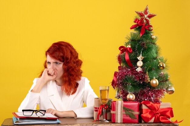 werkneemster zittend achter tafel met kerstcadeautjes en boom op geel