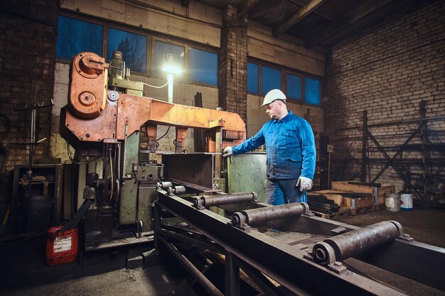 Werknemer bestuurt een proces van railsnijden in een drukke metaalfabriek.