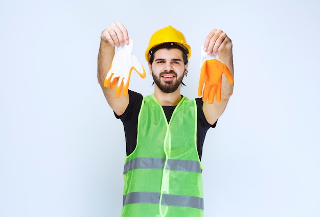 Gratis foto werknemer in gele helm die zijn werkplaatshandschoenen uithaalt en demonstreert.