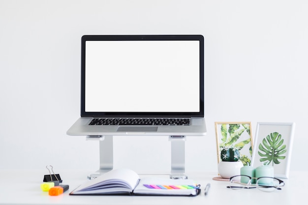 Werkplek met laptop op standaard in de buurt van brillen, Kladblok en fotolijsten