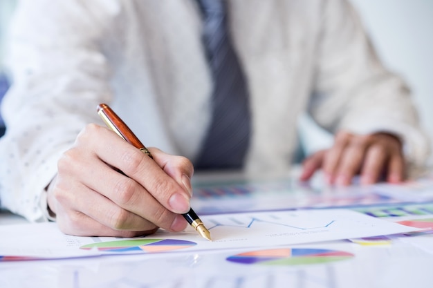 Werkproces opstarten. Zakenman werken aan de houten tafel met nieuw financieel project. Moderne notitieblok op tafel. Pen houdende hand