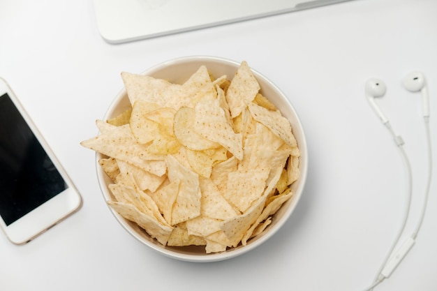 Werkruimte met laptop verfrommeld papier briefpapier en chips op witte tafel Slechte gewoonten concept