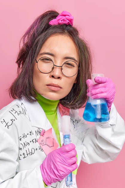 wetenschapper voert chemisch experiment uit houdt glazen kolven met vloeistof vast maakt brede discretie op het gebied van geneeskunde kijkt aandachtig naar camera draagt witte jas rubberen handschoenen werkt in laboratorium