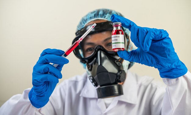 Wetenschappers die maskers en handschoenen dragen Een spuit met een vaccin vasthouden om covid-19 te voorkomen