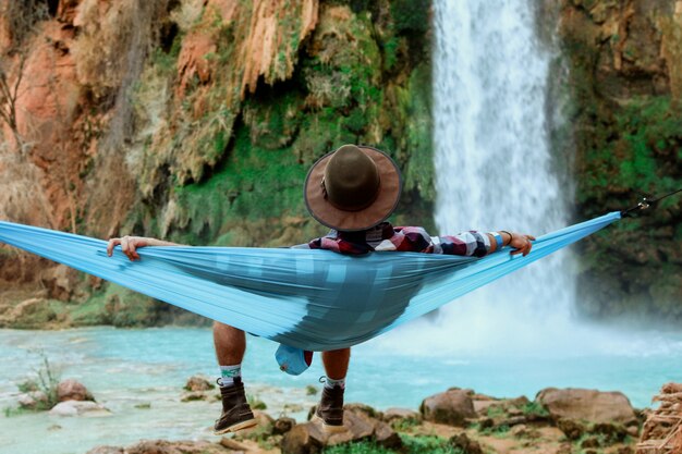 Wide shot van een man liggend op een hangmat naast een waterval stroomt naar beneden van een heuvel