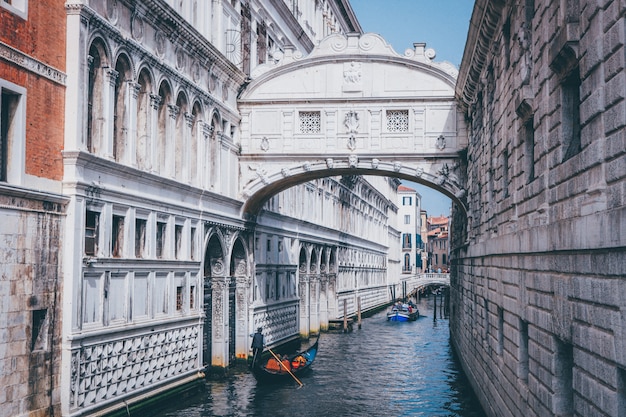 Wide shot van een persoon die een gondel op een rivier onder de brug der zuchten in Venetië, Italië roeien