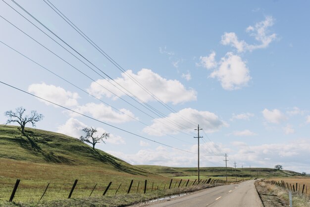 Wide shot van een snelweg weg in de buurt van groene heuvels onder een heldere blauwe hemel met wolken
