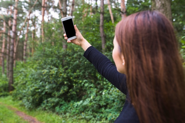 Gratis foto wijfje die selfie door cellphone in het bos nemen