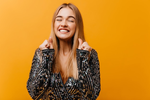 Winderige vrolijke vrouw die van portretshoot op sinaasappel geniet. Sierlijke blonde vrouw lachend met gesloten ogen.