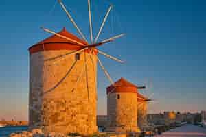 Gratis foto windmolens aan de oever van de baai tijdens zonsondergang in de stad rhodos op het eiland rhodos van het eiland van de dodekanesos archipel europevacation en populaire reisbestemming