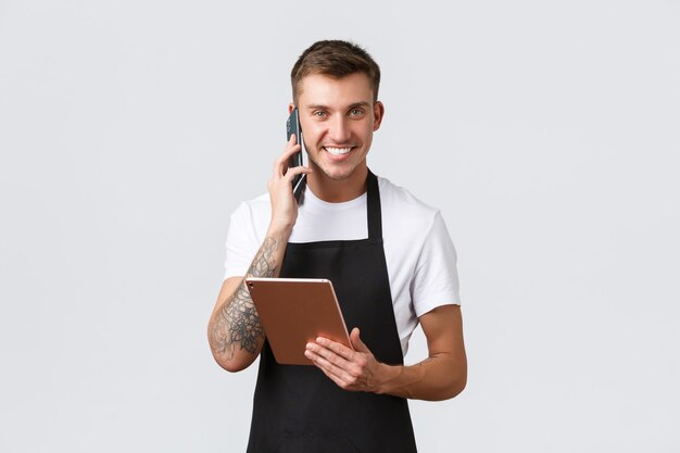 Winkels, kleine bedrijven, café en restaurants afhaalconcept. Knappe glimlachende verkoper, barista die aan de telefoon praat, blij lacht, bestelling opneemt voor levering, digitale tablet vasthoudt