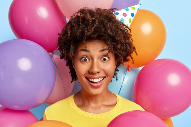 Winsome jonge vrouw poseren omringd door kleurrijke verjaardagsballons