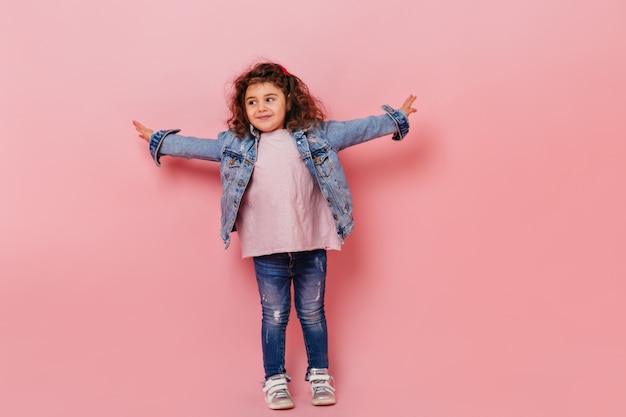 Winsome preteen meisje gelukkige emoties uitdrukken. Zalige brunette jongen in spijkerbroek poseren op roze achtergrond.