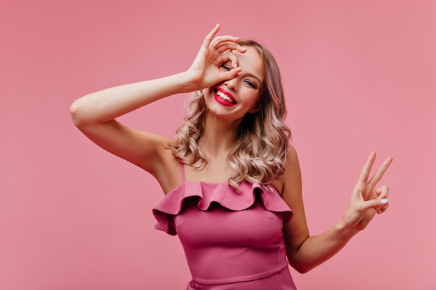 Winsome vrouw met blond golvend haar gek rond op roze muur