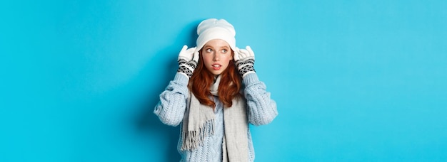 Gratis foto winter- en vakantieconcept schattig roodharig meisje dat naar buiten gaat, muts en handschoenen aan en naar links kijkt