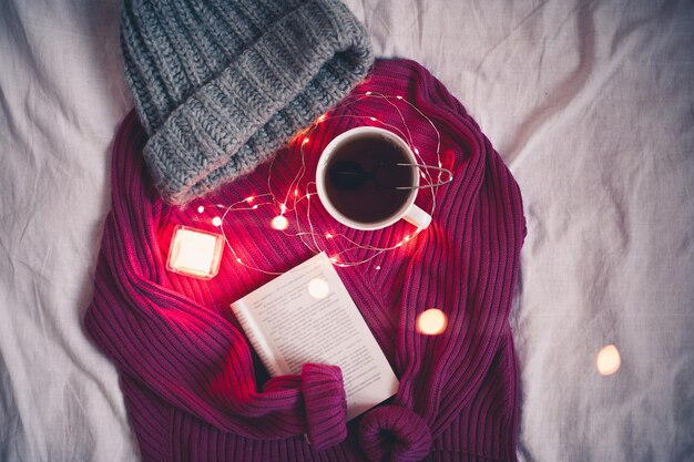 Winterconcept. mok met hete thee, open boek en gebreide trui in bed close-up. goedemorgen. bovenaanzicht.