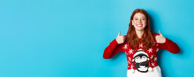 Gratis foto wintervakantie en kerstavond concept gelukkig lachend meisje met rood haar duimen opdagen in appr