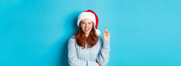 Gratis foto wintervakantie en kerstavondconcept hoopvol roodharig meisje in kerstmuts die een wens doet op xmas cros