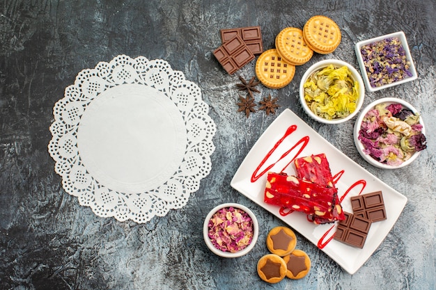 Wit kant met een plaat van chocolade met droge bloemen en koekjes op grijze achtergrond