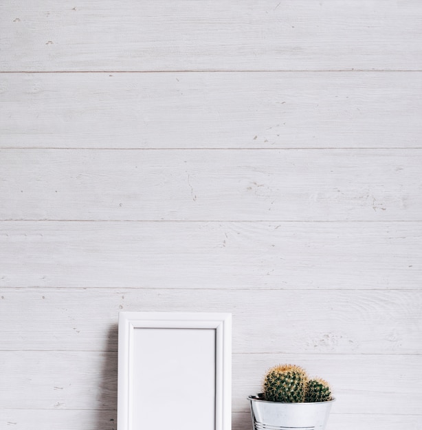 Gratis foto wit leeg frame en cactusinstallatie tegen houten achtergrond