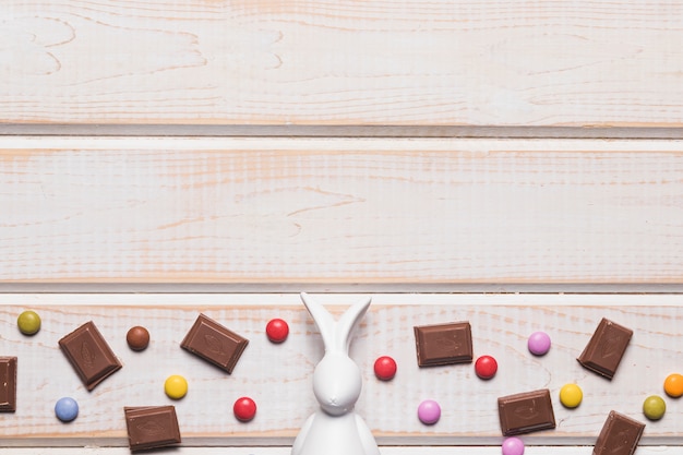 Wit pasen-beeldje in het midden van chocoladestukken en gemuikergoed op houten achtergrond