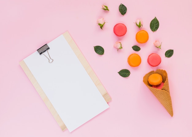 Witboek op klembord met kleurrijke bitterkoekjes over de wafelkegel tegen roze achtergrond