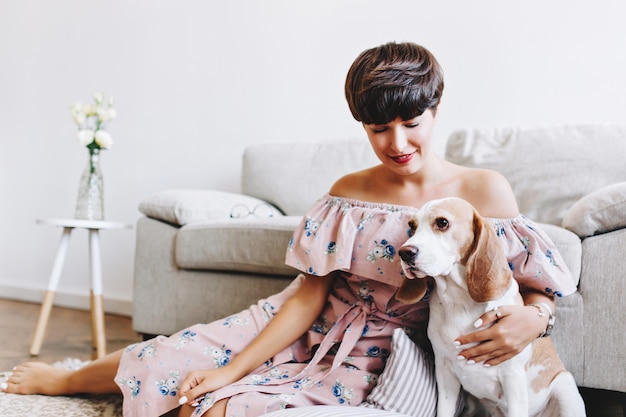 Witte beagle hond met bruine oren wegkijken terwijl glimlachend brunette meisje zit naast